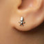 A close-up of a person's ear wearing a small silver earring with a small figure on it.