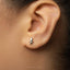 A close-up of a person's ear wearing a small silver earring with a small figure on it.