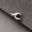 A close-up black and white image of a silver earring or ear cuff resting on a textured gray surface.