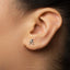 A close-up of a person's ear with a small silver earring featuring a figure of a person.