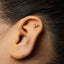 A close-up of a person's ear with a small gold earring in the earlobe.