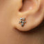 A close-up of a person's ear with a small, silver earring featuring a floral design.