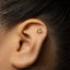 A close-up of a person's ear with a small gold-colored earring in the earlobe.