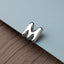A silver letter 'M' is placed on a light blue surface.