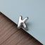 A silver letter 'K' is placed on a textured surface, such as a piece of fabric or a wooden background.
