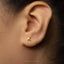 A close-up of a person's ear with a small gold letter K earring.