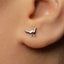 A close-up of a person's ear with a small silver earring featuring a bird design.