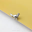 A silver metal pin in the shape of a bird is resting on a yellow surface.