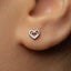 A close-up of a person's ear with a small heart-shaped earring in the earlobe.