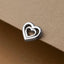 A silver heart-shaped charm or pendant is resting on a textured surface.