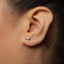 A close-up of a person's ear with a small silver earring featuring a bird design.