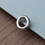 A shiny silver ring is resting on a textured surface, with a light blue background.