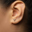 A close-up view of a person's ear, showing a small, triangular-shaped earring with a geometric design.