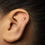 A close-up of a person's ear with a small gold 7-shaped earring in the earlobe.
