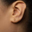 A close-up view of a person's ear with a small gold-colored earring in the earlobe.