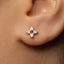 A close-up of a person's ear with a small silver earring featuring a cross-shaped design.
