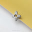A silver-colored metal charm or brooch with a cross-shaped design is placed on a yellow surface.