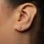 A close-up of a person's ear with a small silver earring featuring a cross-shaped design.