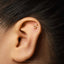 A gold earring with a Taurus symbol is visible in the ear of a person with dark hair.
