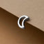 A silver earring in the shape of a crescent moon is resting on a brown surface.
