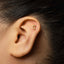 A close-up of a person's ear with a small gold earring featuring a crescent moon design.