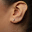 A close-up view of a person's ear with a small silver earring featuring a musical note design.