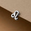 A silver-colored metal charm in the shape of a zodiac sign, specifically a Leo symbol, is attached to a piece of paper.