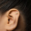 A close-up of a person's ear with a small gold earring in the earlobe.