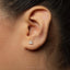 A close-up of a person's ear with a small, diamond-encrusted earring in the earlobe.