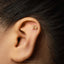 A gold earring with the astrological sign symbol is visible in the ear of a person with dark hair.