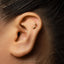 A close-up of a person's ear with a gold-colored earring featuring a musical note design.