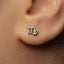A close-up of a person's ear with a small silver earring featuring the astrological sign symbol for Capricorn.