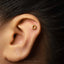 A close-up of a person's ear with a small gold earring featuring a letter "D" in the center.