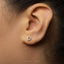 A close-up of a person's ear with a small silver earring featuring the letter 'D' in the shape of a letter.
