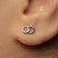A close-up view of a person's ear with a small silver earring featuring a pair of interlocking rings.