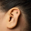 A close-up of a person's ear with a small gold-colored earring in the earlobe.