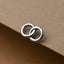 A silver earring with two intertwined rings is displayed on a brown surface.