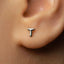 A close-up of a person's ear with a small silver earring featuring a letter 'T' in the center.