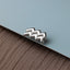 A silver earring in the shape of the Aquarius zodiac sign is resting on a textured surface.