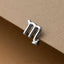 A silver-colored metal letter "M" is attached to a brown surface.