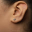 A close-up of a person's ear with a small silver earring featuring a small lip design.
