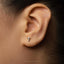A close-up of a person's ear with a small silver earring featuring a letter 'T' in the center.