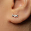 A close-up of a person's ear with a small silver earring featuring a bow design.