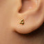 A close-up of a person's ear with a small gold earring featuring the number 4.