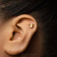 A gold earring in the shape of a watering can is visible in the person's ear.