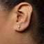 A close-up of a person's ear with a small, silver earring in the earlobe.