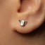 A close-up of a person's ear with a small silver earring shaped like a watering can.