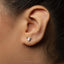A close-up of a person's ear with a small silver earring shaped like a watering can.