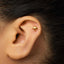 A gold earring in the shape of an umbrella is visible in the person's ear.