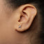A close-up of a person's ear with a small silver earring featuring a zodiac symbol in the earlobe.
